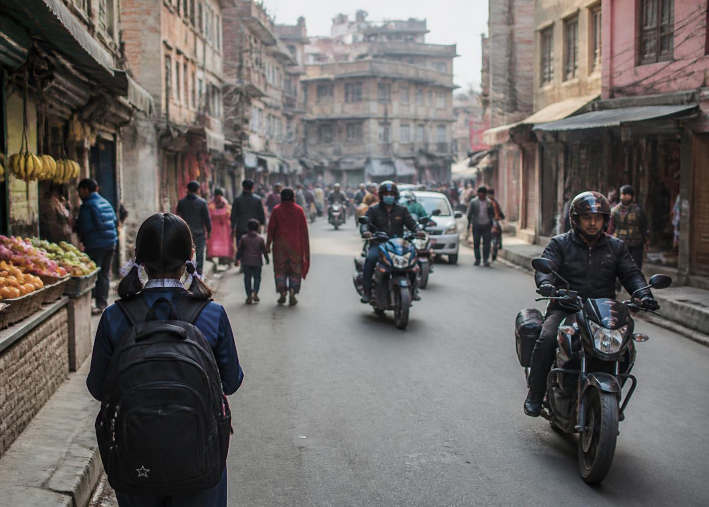 A student walking through a busy neighbourhood street in Kathmandu